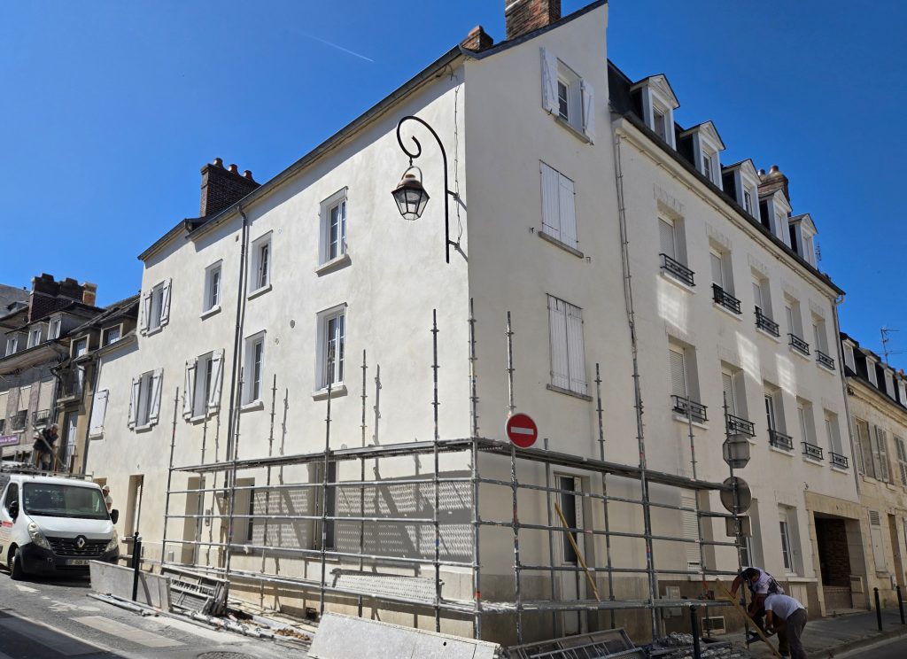 Équipe en plein chantier de ravalement de façade sur un grand immeuble d'angle en centre-ville avec échafaudage sur rue à Compiègne.